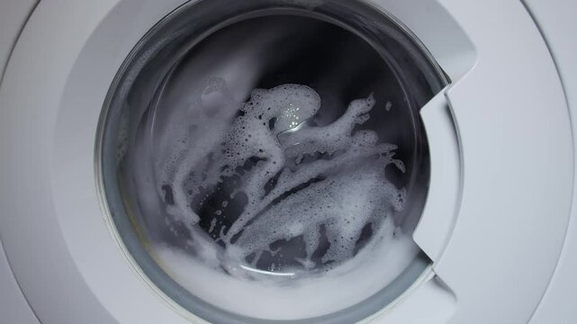 Inside a washing machine, clothes spin in soapy water. Closeup view