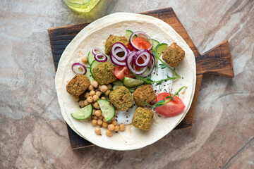 Wheat wraps with falafel, vegetables and yogurt on a brown granite background, horizontal shot, view from above