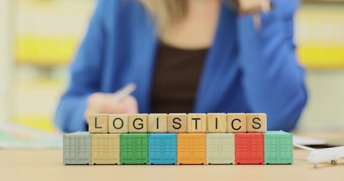 Woman talks with workmates at desk with blocks showing Logistics on small containers. Concept related to supply chain management and transportation