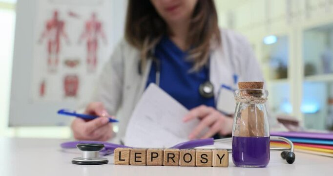 Wooden blocks with Leprosy on desk and female doctor in coat writing on document. Medical context related to treatment of leprosy in modern clinic