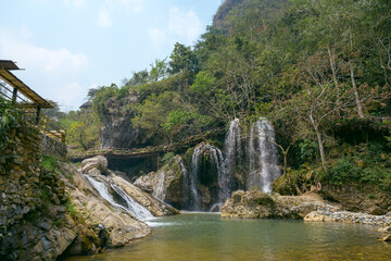 Obraz premium A peaceful waterfall surrounded by rocks and green forest in Cat Cat Village, Sapa, Vietnam. A popular destination for nature lovers.