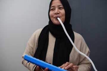 Asian muslim woman playing pianica, melodica blow organ musical intrument