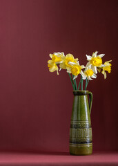 Atmospheric still life with daffodils in dark vase on dark background. Copy space . Suitable for illustration of spring mood, floristics.