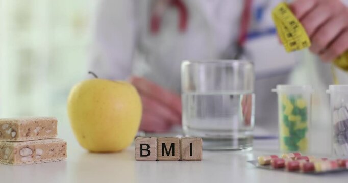 Female doctor writes patient data at desk with blocks with BMI near apple and water. Concept of body mass index suggesting focus on healthy lifestyle