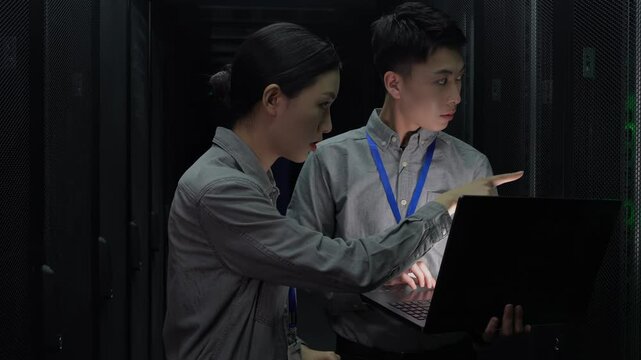Two smart engineers IT technicians using laptop checking open rack server cabinet updating hardware cooperating in futuristic digital room of data center with rows of server racks super computers