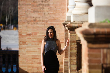 young and beautiful brunette woman in elegant black dress is in the famous square of spain in...