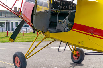 small yellow and red plane at the airport. plane standing on the runway with a view of the pilot's cockpit through the open door. beautiful sunny day.