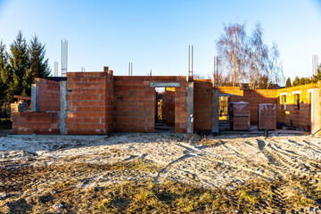 Unfinished brick building under construction on sandy ground with rebar and building materials around, illustrating housing development process