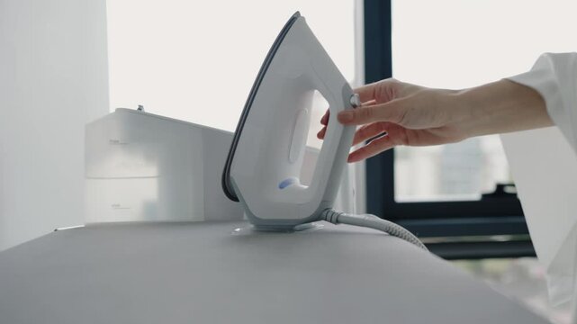 A modern steam iron rests on an ironing board near a window in a minimalist home setup. The image captures the essence of domestic chores in a contemporary household environment.