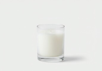 A clear glass candle holder filled with white wax on a white surface in a minimalist setting