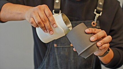 A barista is preparing matcha. He is holding two cups in his hands and pouring the drink from one to the other. Closeup.  Soft focus
