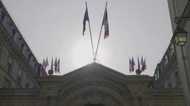 Building exterior of Banque de France in Paris with French flags under the sun