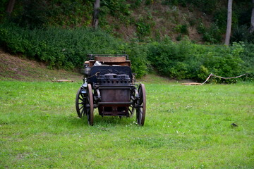 A close up on a cart or automobile used by military forces in order to transport food, drinks and key equipment to soldiers seen standing on a field, next to a grass covered hill and moor or forest