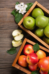 Ripe red and green apples with branch of white flowers in wooden box on a wooden table