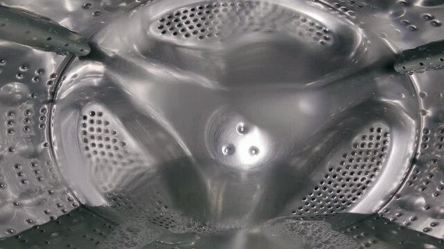 View from inside the drum of a washing machine with perforated holes, centre agitator and water during operation. Time-lapse. Close-up