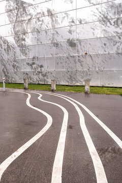 Curved white road lines create a visual flow on smooth asphalt near a modern glass building, ideal for concepts of guidance, navigation, and urban infrastructure clarity.
