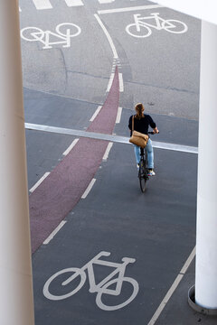 Cyclist riding over white bike lane icons on marked asphalt under columns, symbolizing safe cycling infrastructure and sustainable city transportation.