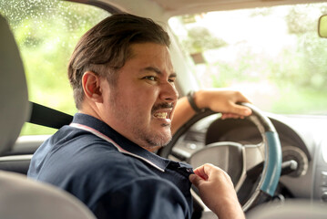 Middle-aged man in the driver’s seat tugs at his shirt collar, showing visible discomfort from...