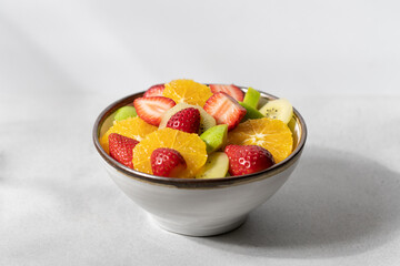 Fruit salad in bowl on white background. Strawberry, orange, apple, banana, kiwi healthy summer salad