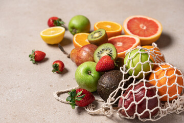 Variety of fruits and berries pouring out of mesh bag. Orange, grapefruit, avocado, lemon, kiwi, apple, pear and ripe strawberries
