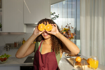 Woman in a kitchen playfully covering her eyes with orange halves