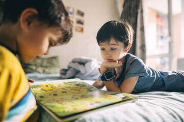 Brothers reading a book together at home in a cozy bedroom setting