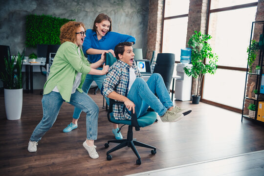 Group of colleagues having fun in the office rolling on a chair, showcasing teamwork and camaraderie in a modern workplace setting. - Powered by Adobe