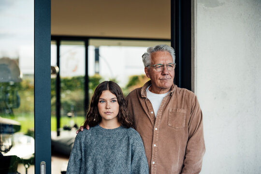 Grandfather and granddaughter standing together indoors by a window