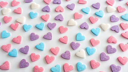 Fototapeta premium Colorful heart-shaped candies are scattered across a white surface