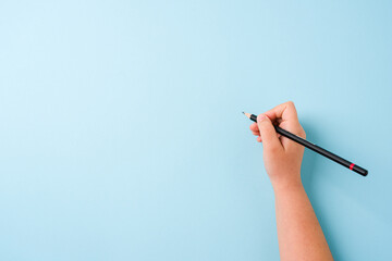 Girl holding pencil with right hand on blue background © yalcinsonat