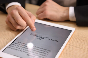 Electronic signature. Man using tablet at wooden table, closeup
