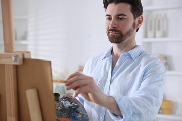 Fototapeta premium Man painting picture on easel in artist's studio