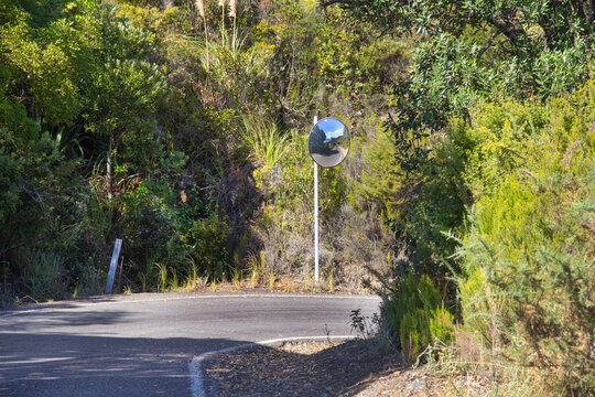 Convex mirror on a tight narrow one-lane road bend at Rings Beach, Coromandel Peninsula, New Zealand. Safety measure for blind curves.