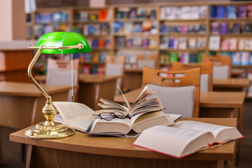 Different books, glasses and beautiful lamp on wooden desk in library