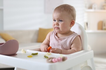 Cute little baby eating on feeding chair at home. Space for text