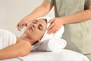 Young woman receiving facial massage with gua sha tool in spa salon