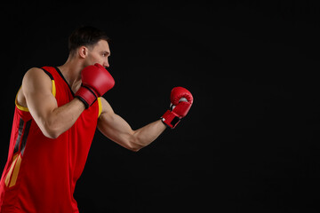 Man in boxing gloves fighting on black background, space for text