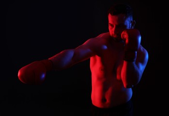 Man in boxing gloves fighting on black background in neon lights