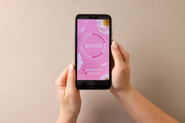 Menstruation. Woman holding smartphone with period calendar application on beige background, top view