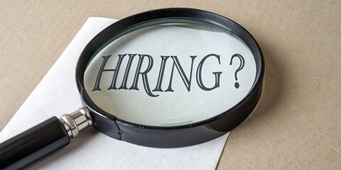 Job Market Competition Concept. Magnifying glass focuses on "HIRING?" text on paper.