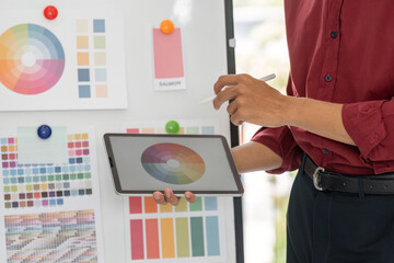 Color Theory and Design Collaboration. A designer holds a tablet showcasing color palettes during a...