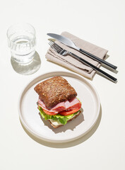 Toast sandwich made of grain bread with prosciutto, tomatoes, lettuce and sauce on light background