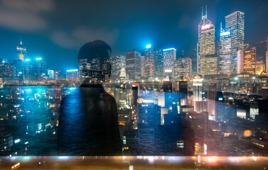 Naklejka premium Night view of Hong Kong skyline using double exposure technique, creating an ethereal and layered image of the vibrant cityscape and a figure gazing out.