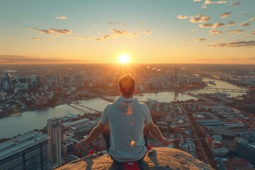 Man meditates on a rock overlooking the city at sunset with a vibrant skyline and river below