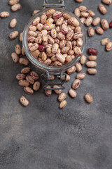 Glass jar full of dried pinto beans on gray top view, copy space. Traditional Latin American legumes
