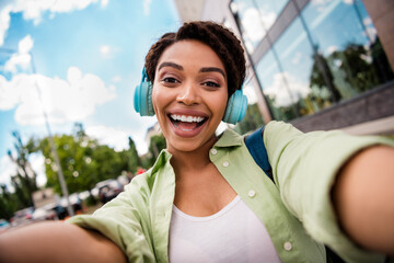 Cheerful young woman taking a joyful selfie with headphones in urban setting