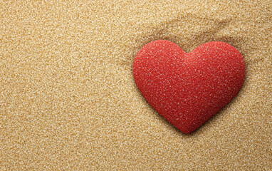 A heart shape made of pebbles on a textured sandy background.