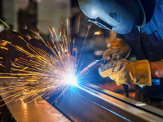  A worker manually welds steel and stainless steel components using TIG technology, detail of an electric arc