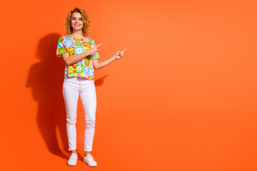 Happy woman wearing a floral print shirt gestures towards empty orange background for advertising