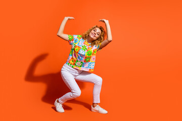 Cheerful young woman posing playfully with raised arms against a vibrant orange background in casual spring attire